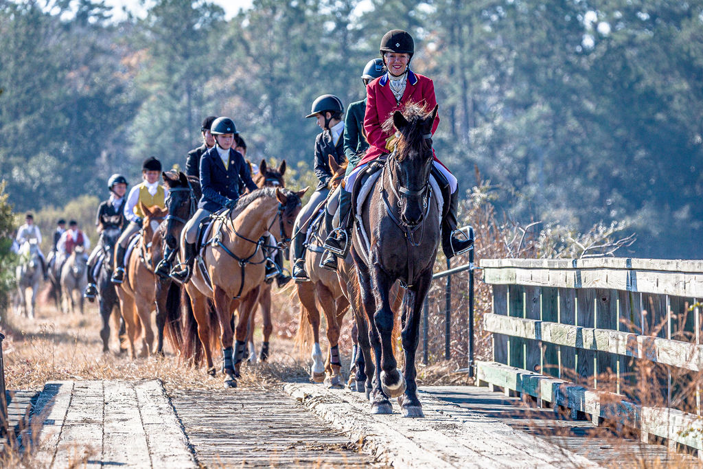 A mounted field crossing a wooden bridge in a long line.