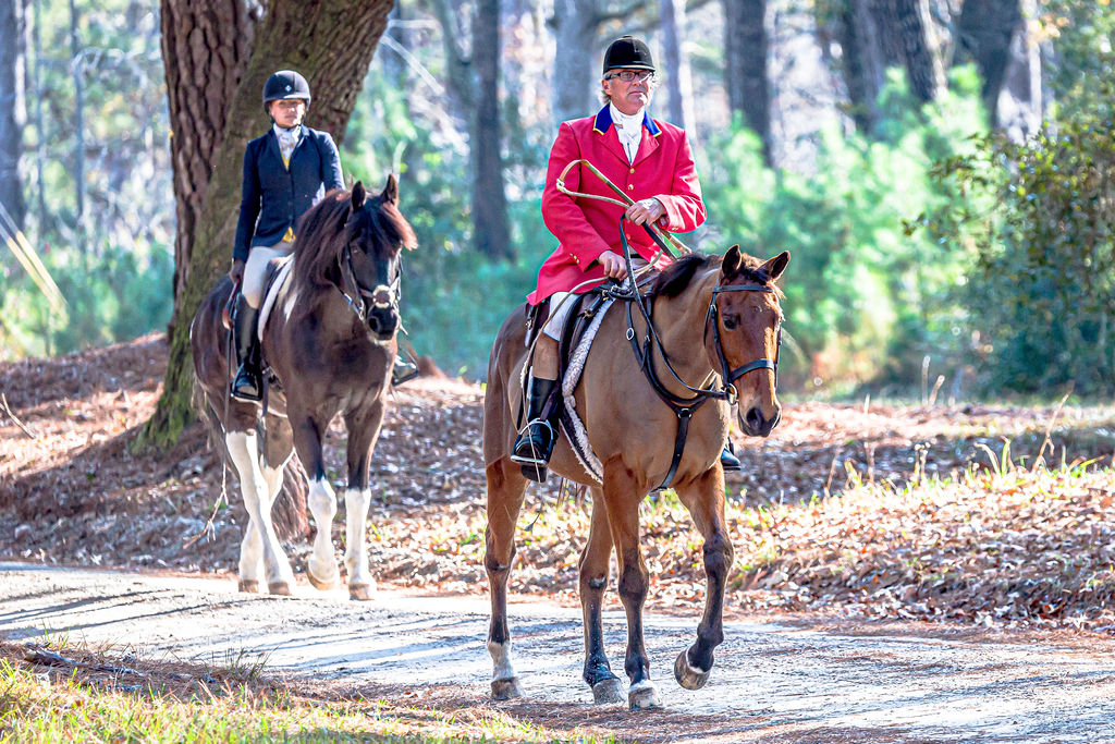 Two mounted riders moving along a wooded track.