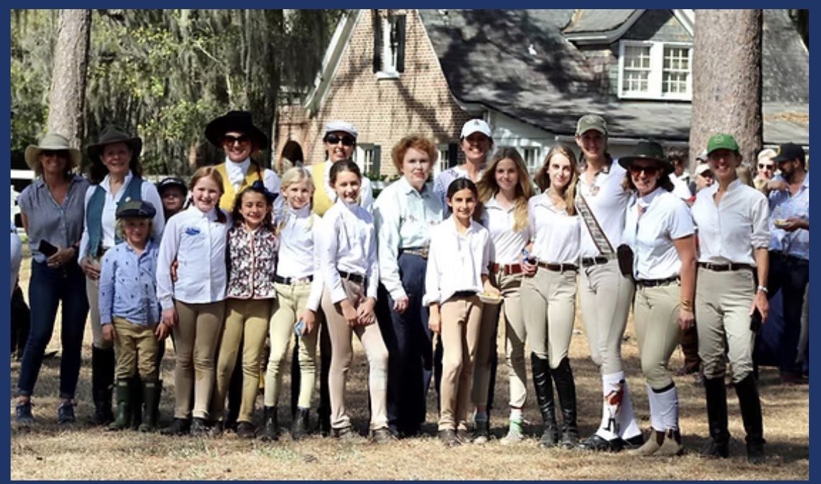 A wide group of adult and junior club members gathered together outdoors.