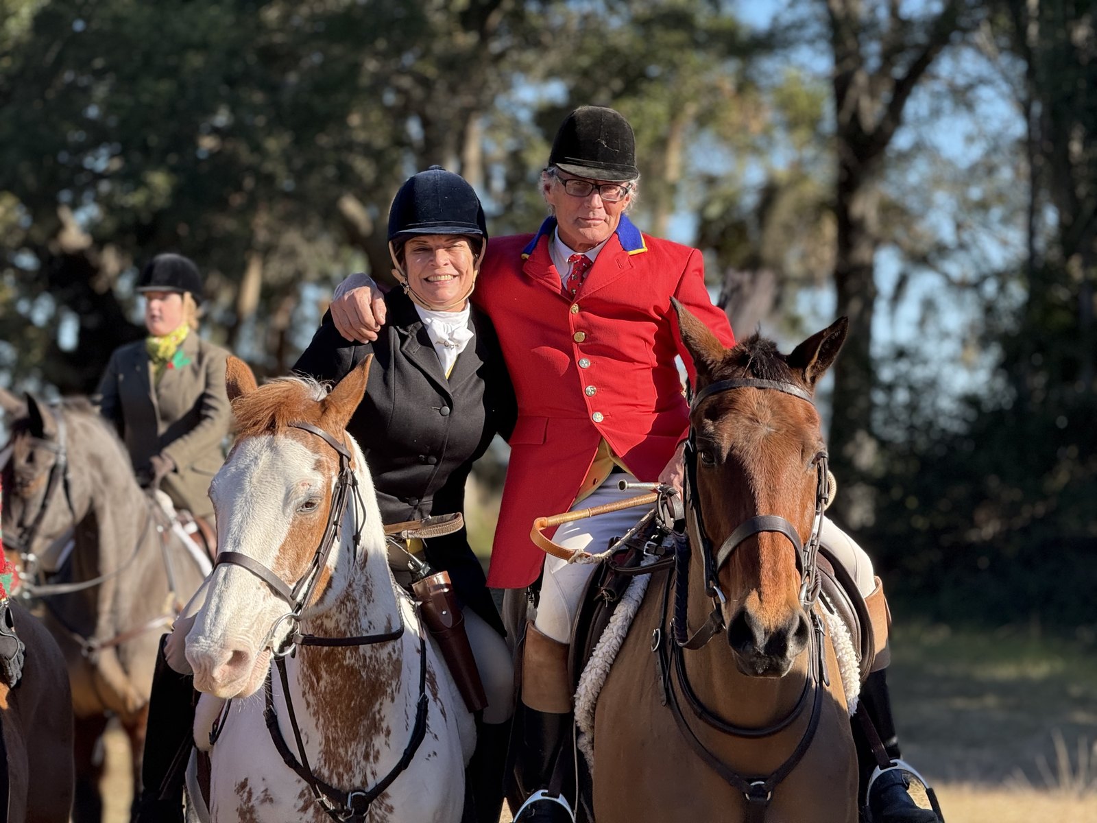 Two mounted members side by side at the meet, one in a scarlet coat and one in black, with riders behind them.