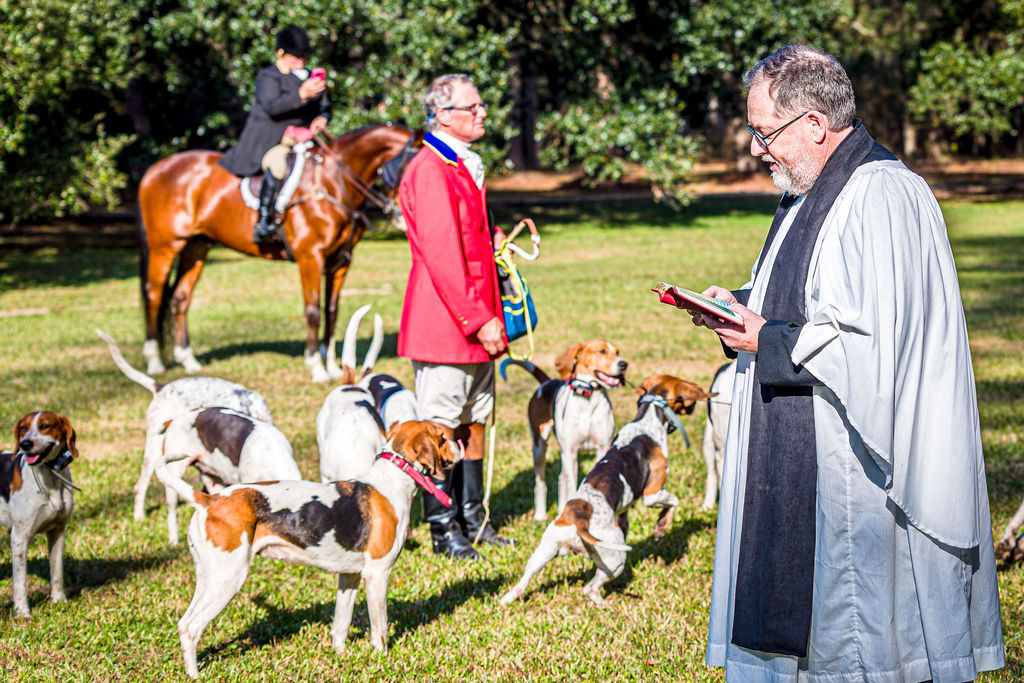 A clergyman reading beside gathered hounds and mounted members of the Hunt.