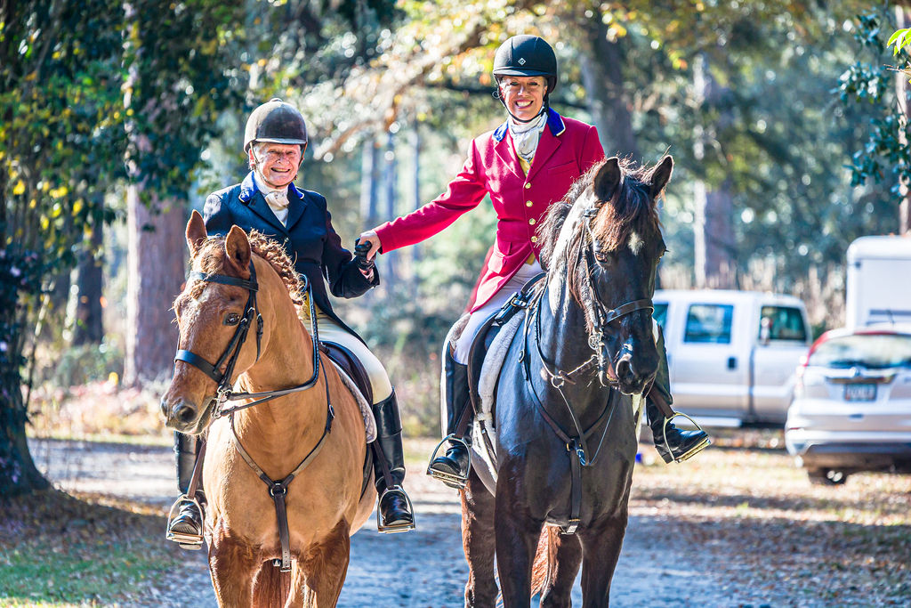 Two mounted riders greeting one another at a woodland meet.