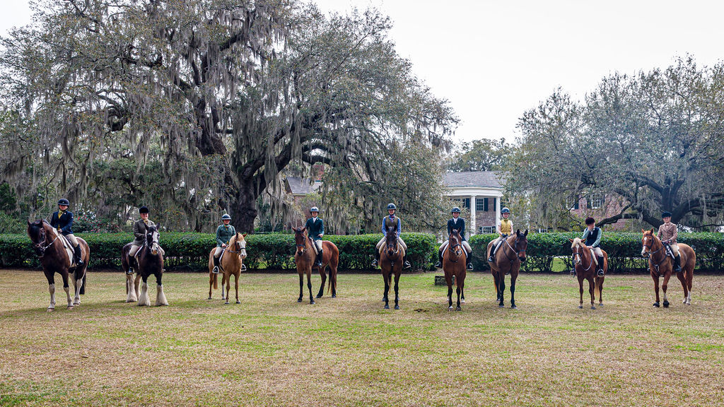 Junior riders mounted in a line beneath live oaks.