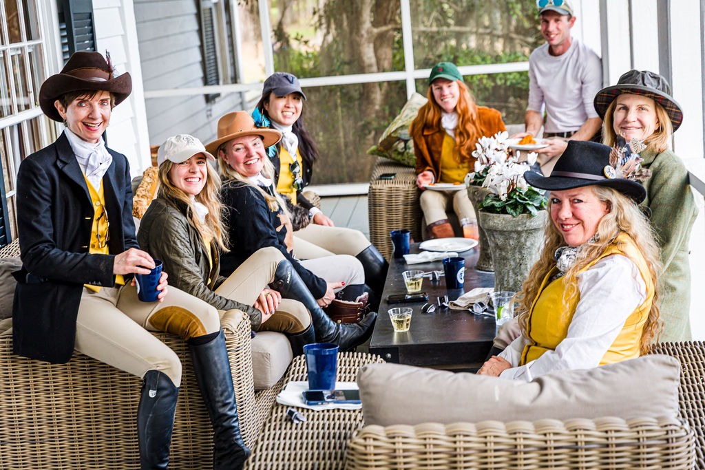 Club members in riding clothes gathered around a table on a screened porch.